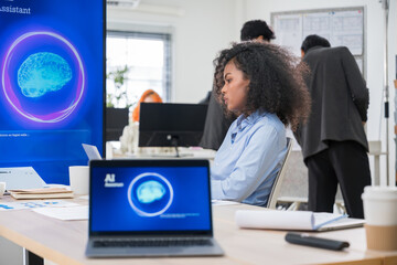African American businesswoman in modern office using laptop and smartphone voice recognition with AI assistant technology to improve communication, multitasking, and workplace productivity.