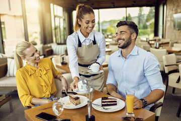 Waitress serving coffee to a smiling couple at a restaurant with cake and orange juice on the table