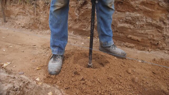 arborist preparing planting site, arborist in denim boots carefully digging planting hole with auger, focused arborist in denim and boots is digging measured planting hole with auger in soft