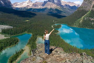 A girl is pointing at mountain lake and forest view from the top of the cliff.