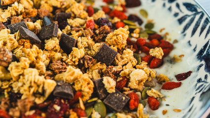 Beautiful yogurt bowl with crunchy granola, chocolate pieces, pumpkin seeds, goji berries and chia seeds. Perfect healthy breakfast or snack with a tasty indulgence.