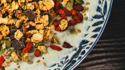 Beautiful yogurt bowl with crunchy granola, chocolate pieces, pumpkin seeds, goji berries and chia seeds. Perfect healthy breakfast or snack with a tasty indulgence.