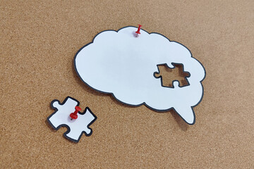 Missing puzzle piece completing a brain symbol on a cork board. Mental health and problems with memory.