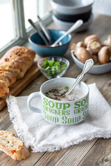 Above view of a cup of cream of mushroom soup served with a crusty baguette.