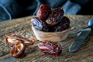 A small wooden bowl of medjool dates with a cut one and a whole on in front.