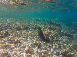 Underwater rocky seabed with clear turquoise water and sun rays in Calanques National Park, near Marseille, France.