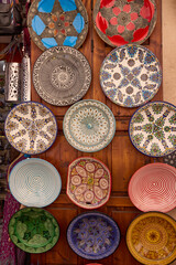 A variety of colorful, handcrafted plates decorate a wooden surface in Morocco. The plates have different patterns and colors, showcasing Moroccan artistic style