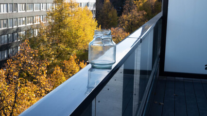 A broken glass jar on a balcony railing, with yellow autumn trees below.