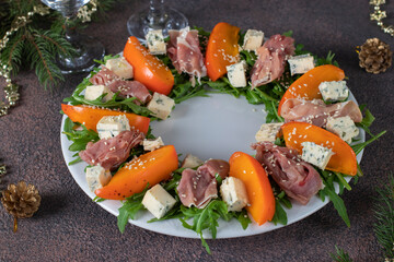 Salad with hamon, persimmon, arugula and dor bleu cheese on white plate