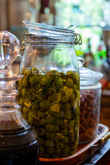A large glass jar of green olives marinating in olive oil with sliced garlic and rosemary makes an elegant bar snack. Graphic resource