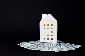 White ceramic house model placed on a pile of cash, symbolizing real estate investment and financial growth in a modern context. copy space