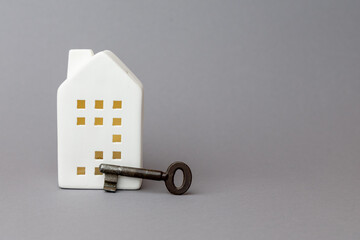 White ceramic house model with key beside it, symbolizing finance, investment, and home ownership in a minimalist setting. copy space