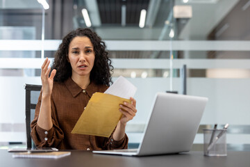 Fototapeta premium Young professional woman feeling upset and confused after opening a critical document from a brown envelope at her desk. Processing unexpected information during a difficult moment in her business day