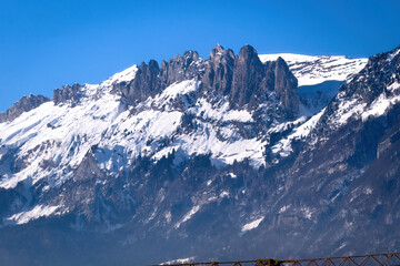 Obraz premium The rugged cliffs of Saxer Gap (Saxer Lücke) rise dramatically above the snowy slopes of the Alpstein massif on a clear winter day in eastern Switzerland against blue sky