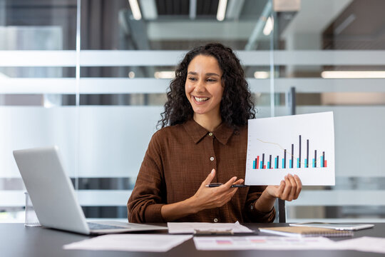 Young businesswoman with curly hair presenting a bar chart with a positive trend during an online meeting or video call, working remotely from an modern office