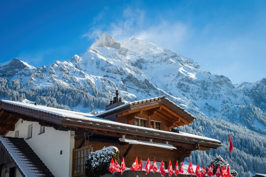 Adelboden, Switzerland - January 12, 2025: A traditional Swiss chalet decorated with national flags for Ski Alpine World Cup at Chuenisb&auml;rgli with Lohner Mountains in the background against blue sky