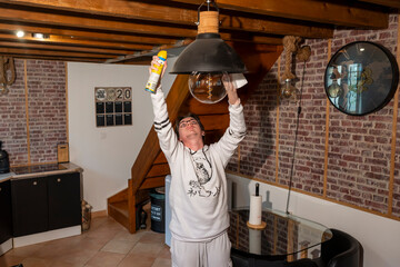 jeune homme faisant son ménage et nettoyant le dessus d'un plafonnier