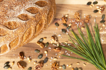 Close-up of rustic artisan bread with leaf pattern, surrounded by chives, sea salt, walnuts, pumpkin and pine seeds on vintage wooden surface. Perfect background for bakery and healthy food.