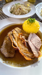 Hearty Bavarian-style roast pork Schweinsbraten served with potato dumpling and rich gravy, accompanied by cabbage salad