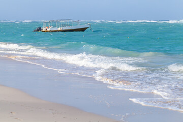 A small motor boat floats off a white sandy beach as turquoise waves