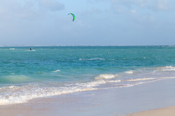 Beach scene with a lone kite surfer glides across turquoise waves