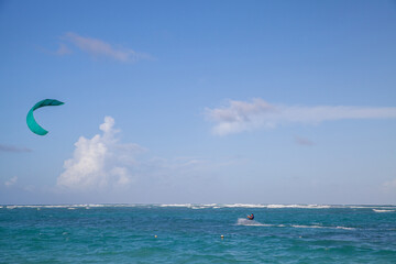A lone kite surfer glides across turquoise waves as a teal kite soars