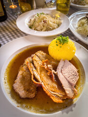 Hearty Bavarian-style roast pork Schweinsbraten served with potato dumpling and rich gravy, accompanied by cabbage salad