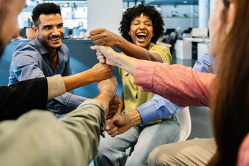 Group of multiracial business colleagues laughing and joining fists together while celebrating at a modern office, showing motivation, friendship, and teamwork. Collaboration and unity concept.