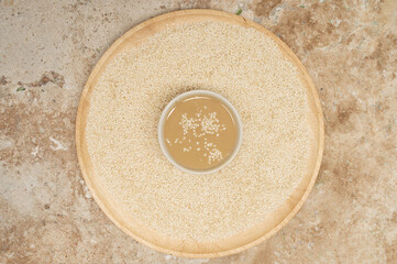 Board with sesame seeds and bowl of tasty tahini on travertine table, closeup