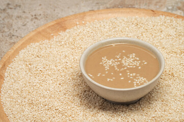 Board with sesame seeds and bowl of tasty tahini on travertine table, closeup