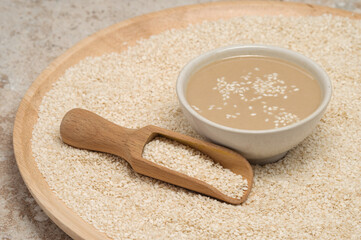 Board with sesame seeds and bowl of tasty tahini on travertine table, closeup