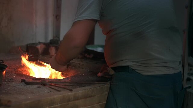 Elderly man in his workshop plates the copper bowl with tin. Tinsmith covering the copper object with tin over fire