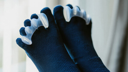 Feet in dark socks with transparent orthopedic toe separators. Bunion relief, foot alignment, hallux valgus support, home therapy, daily foot care, comfortable correction