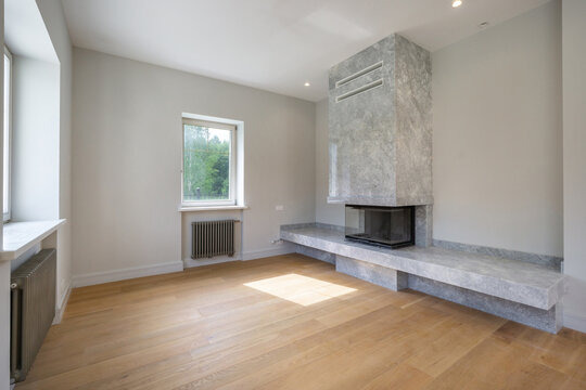 A bright living room features a sleek, stone fireplace and large windows that allow natural light to fill the space. The wooden floor adds warmth to the minimalist decor.