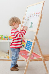 Cute little child playing at a magnetic board, learning letters, numbers and geometric shapes at home. Educative and funny indoor activity for early development.