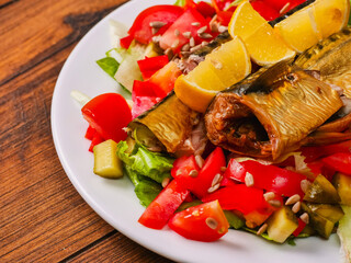 Large plate with fresh lettuce salad, tomato, lemon, sunflower seeds and fine smoked mackerel. Tasty big portion of food served on a wooden table. Healthy diet.