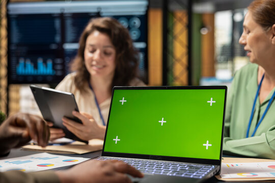 Determined diverse corporate team using laptop with chroma key, exchanging reports and strategy insights with data visualization. Work environment and productivity in office workspace.