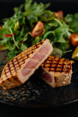 Grille tuna steak served with fresh green salad and cherry tomatoes on a dark plate. Healthy seafood dish, gourmet restaurant meal, fine dining concept.