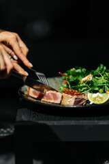 Grille tuna steak served with fresh green salad and cherry tomatoes on a dark plate. Healthy seafood dish, gourmet restaurant meal, fine dining concept.