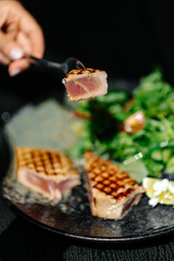 Grille tuna steak served with fresh green salad and cherry tomatoes on a dark plate. Healthy seafood dish, gourmet restaurant meal, fine dining concept.