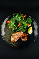 Grille tuna steak served with fresh green salad and cherry tomatoes on a dark plate. Healthy seafood dish, gourmet restaurant meal, fine dining concept.