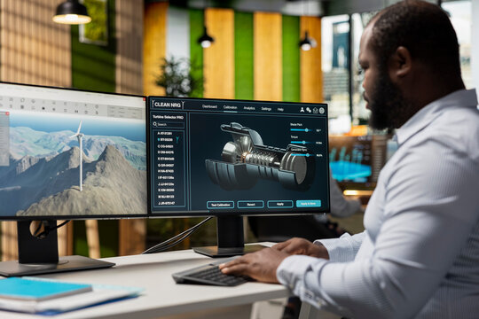 Technician in office analyzes wind turbine component to improve alternative energy efficiency. African american man uses CAD software to refine turbine part design, boosting clean energy output