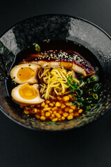 Japanese ramen soup with noodles, soft-boiled egg, grilled pork, corn, and green onions in dark broth. Traditional Asian cuisine, gourmet comfort food.
