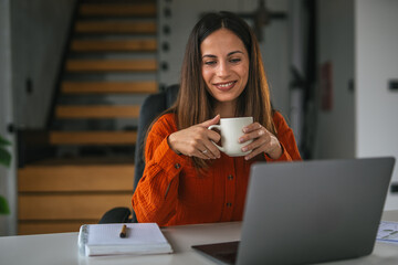 Woman enjoying coffee working remotely on laptop at home