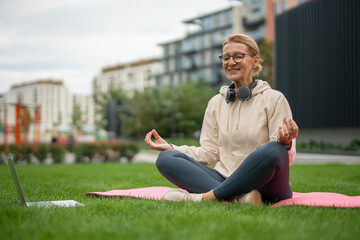 Woman meditating outdoors on yoga mat with laptop
