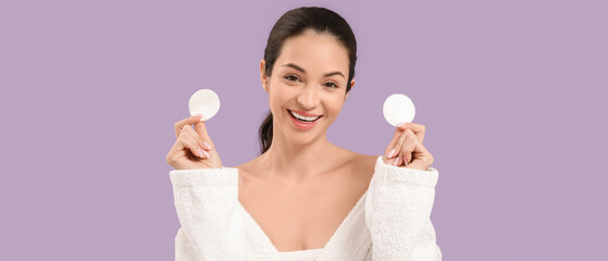 Beautiful young happy woman in bathrobe with cotton pads on purple background