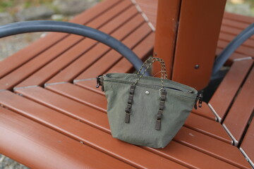 A small green purse is sitting on a brown bench