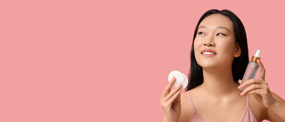 Young Asian woman with cotton pads and bottle of skincare product on pink background, closeup