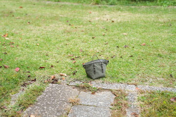 A small green bag is sitting on the grass next to a brick walkway