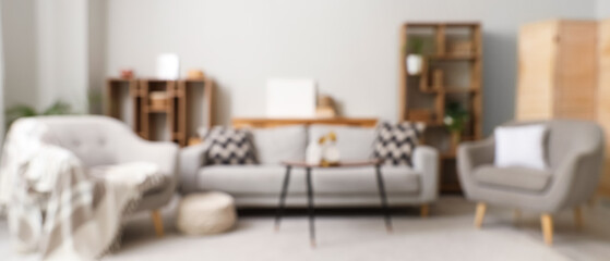 Blurred view of stylish living room with cozy grey armchairs, sofa and coffee table